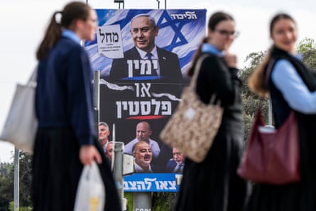 Schoolgirls walk past a Likud campaign billboard featuring Netanyahu’s portrait and Hebrew text