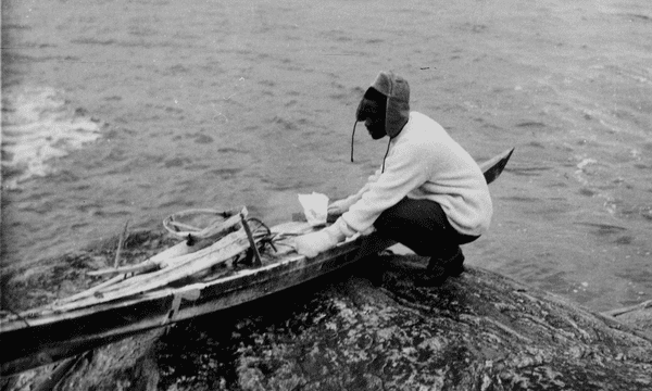 Tété Michel-Kpomassie crouching in the water holding a kayak