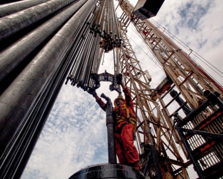 A view upwards at a man in an orange boilersuit carrying out work on pipes