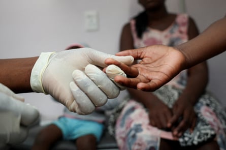 A South African nurse’s hand wearing a latex glove takes a blood sample from a child. Only the hands are in focus.