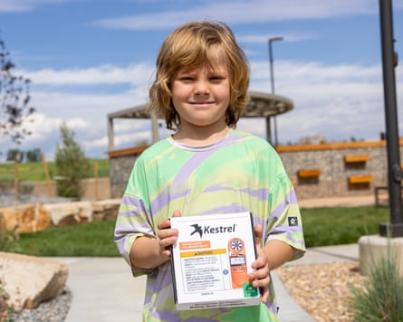 A smiling boy holds up a box in a public garden.