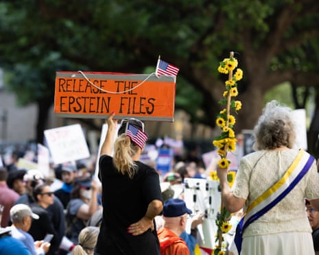 A person in black holds an orange sign reading 'RELEASE THE EPSTEIN FILES' above a crowd at a protest