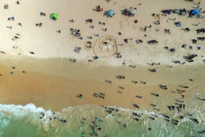 An aerial view of sand sculpture of a horse with people on the beach around it