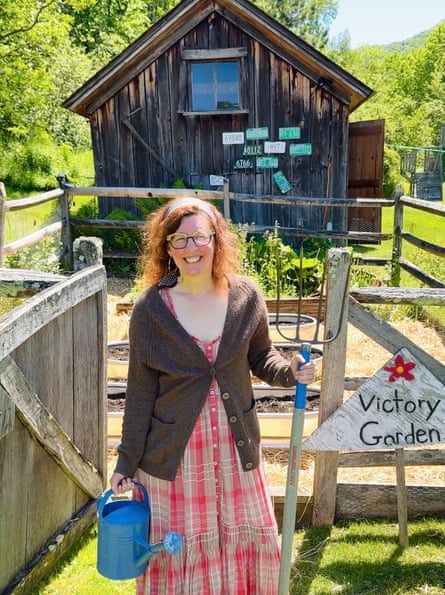 Schaub, holding a garden fork, poses in her garden with a wooden shed behind
