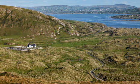 A view over countryside leading down to a bay, with hills visible on a distant coastline.