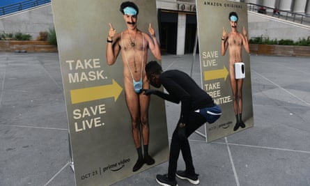 A New Yorker takes a free face mask from a lifesized poster of Sacha Baron Cohen as part of a promotional stunt for Borat Subsequent Moviefilm.