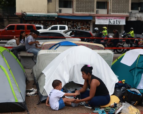 A mother and son sit outside one of a group of tents on a street