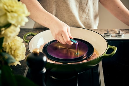 Sebuah tangan memegang pemberat logam bulat untuk meratakan paha ayam yang digoreng dalam wajan.