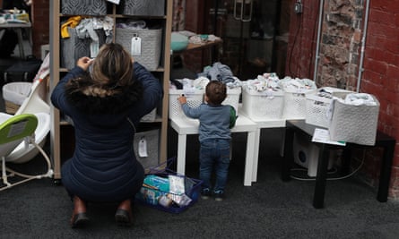 Bir kadın ve yürümeye başlayan çocuk bebek kıyafetleriyle dolu kutulara bakıyor