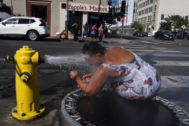 A woman bends down to bury her face in the spray of water from a yellow fire hydrant.