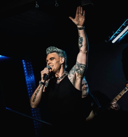 Dan Budd on stage, holding mic in one hand with his other arm raised, showing his tattoos