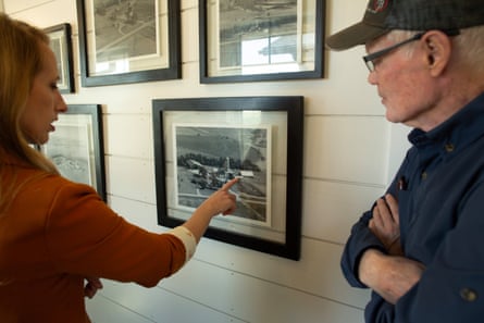 a women pointing to photo of farm building with man in glasses watching