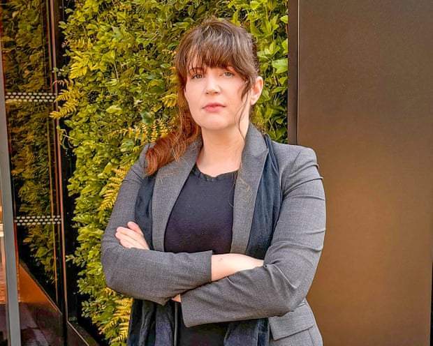 A Women with brown hair and folder arms, in front of foliage