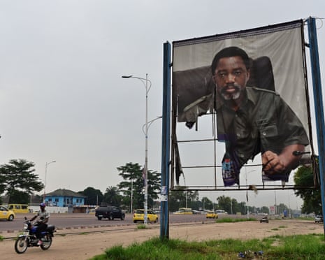 A man rides his motorcycle past a torn portrait of DR Congo's former president Joseph Kabila