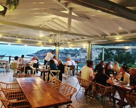 An open-air restaurant with sea views, white roof and wood and wicker furniture