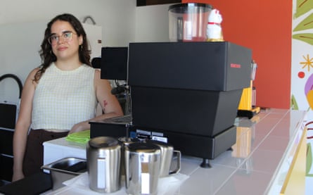 A young Latino woman stands by an espresso machine in a cafe