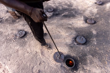 A person lifts a metal lid from one of a line of covered holes using a long metal pole.