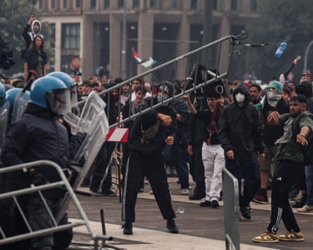 Los manifestantes lanzan una barrera contra un grupo de policías con equipo antidisturbios.