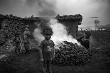Young children blackened with coal dust around a smouldering pile of coal