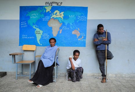 An older woman, and a young woman and man, waiting at what appears to be a school