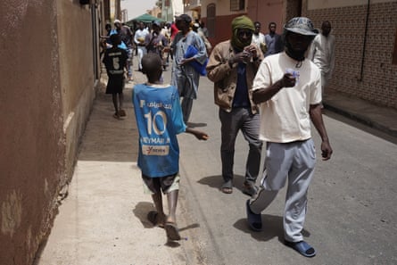 Two boys with a hand outstretched walk past a stream of men on a road