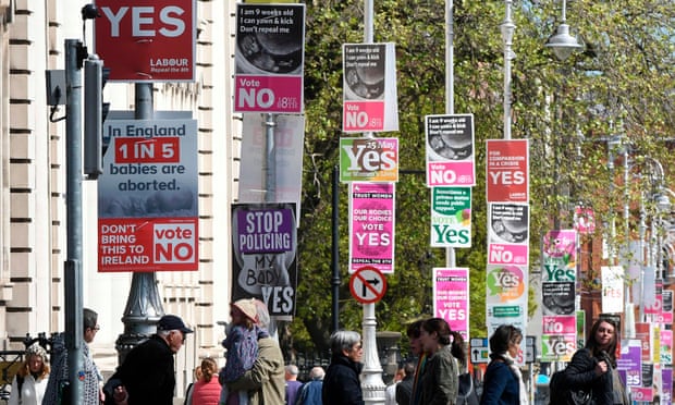 People cross the road past posters urging a yes vote in the referendum to repeal the eighth amendment of the Irish constitution and posters calling for a no vote