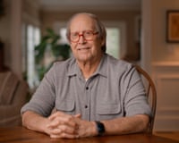 Chevy Chase sits at a table wearing red glasses in a still from the documentary.