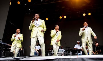four men in green suits on a stage holding microphones