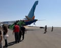 Passengers descend steps from the flydubai plane onto a runway, with military personnel nearby