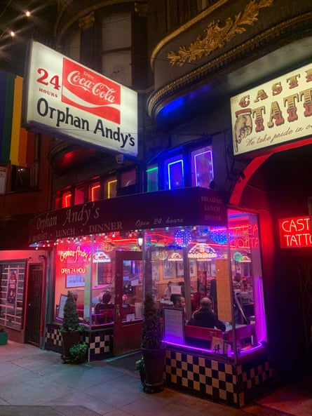 The outside of a diner decorated with rainbow-colored neon lights and people sitting at tables inside
