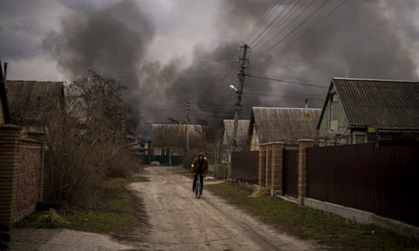 A Ukrainian man rides his bicycle near a factory and a store burning after it had been bombarded in Irpin
