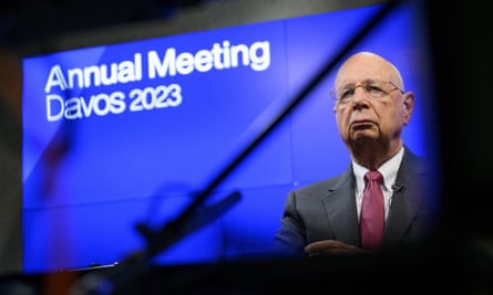 A large video screen displays a portrait of Klaus Schwab with a blue background and a slogan that says