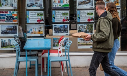 young couple walk past estate agent's window in clapham, south london