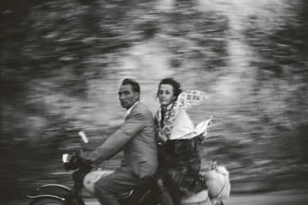 Black and white photograph of a man and a woman on a motorbike against a blurred background.