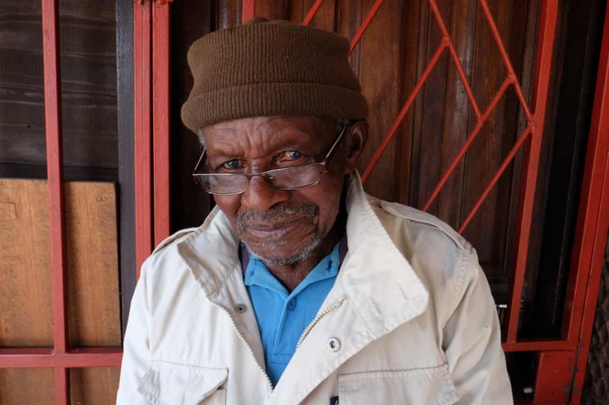 Mofokeng in white coat and brown hat looks at camera