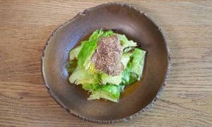 An irregular-shaped round brown plate with a pile of cabbage leaves and truffle in the middle