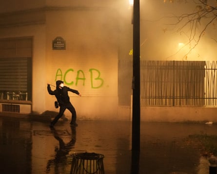 A masked protester throws a projectile near graffiti in a smoky Paris street at night