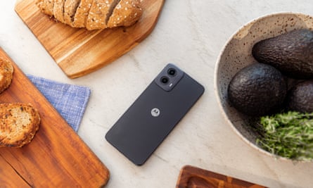 Black Moto G34 phone on a kitchen table surrounded by food
