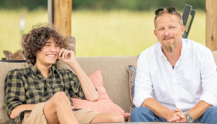 A young boy wearing a plaid shirt and an older man wearing a white shirt, jeans, and sunglasses on his head