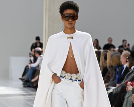 A model in a floor-length ivory cape fastened with a simple gold clasp