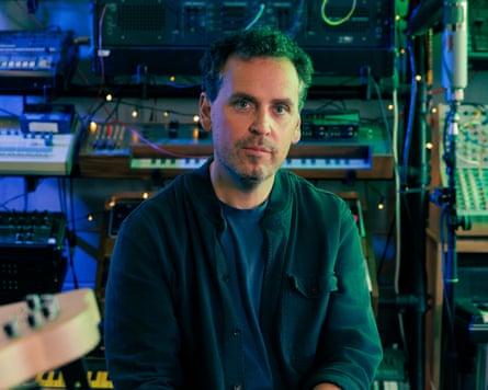 James Ellis Ford sitting in a room in his home in London, surrounded by synthesisers and other electronic equipment