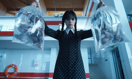 Jenna Ortega as Wednesday Addams, holding two clear plastic bags filled with water and swimming piranhas.