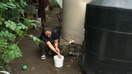 A woman draws water from a large storage tank into a white plastic bucket.