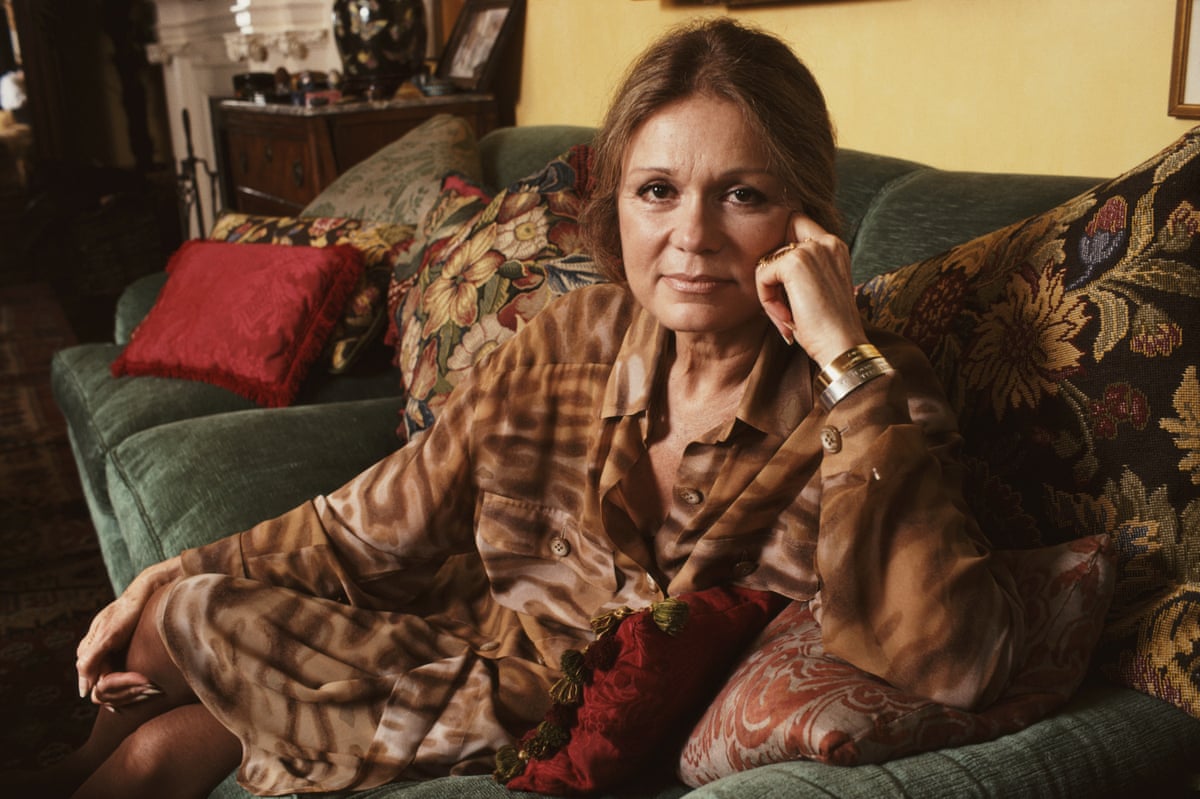 Feminist writer and influencer Gloria Steinem, pictured sitting on a green sofa with patterned cushions in her apartment, November 1990.