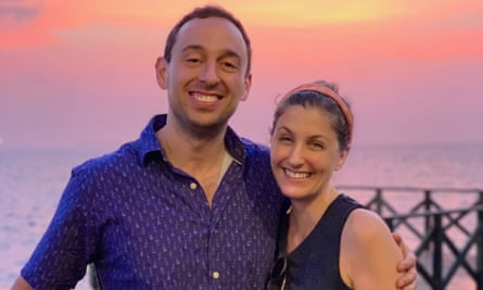 A man and a woman smile in front of a sunsetting sky