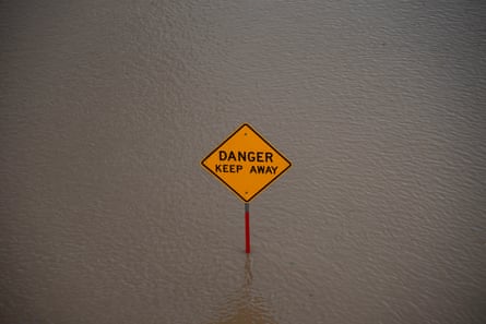 a yellow sign in a flooded river reads ‘danger keep away’