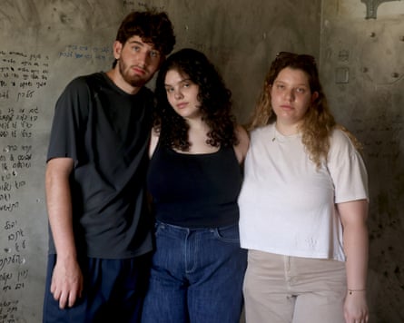 Three Matias siblings standing against an interior wall covered with writing
