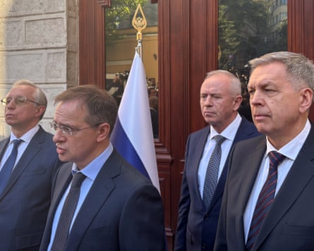 Four men in suits face members of the media