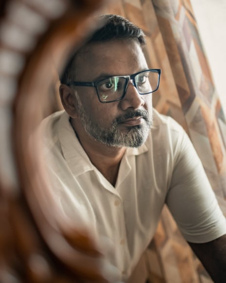 A man with black-rimmed glasses looks into a mirror as he poses for a portrait at home on July 29, 2026 in Noida, India.