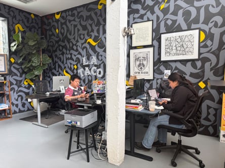 Two people sit in an office at their work stations.